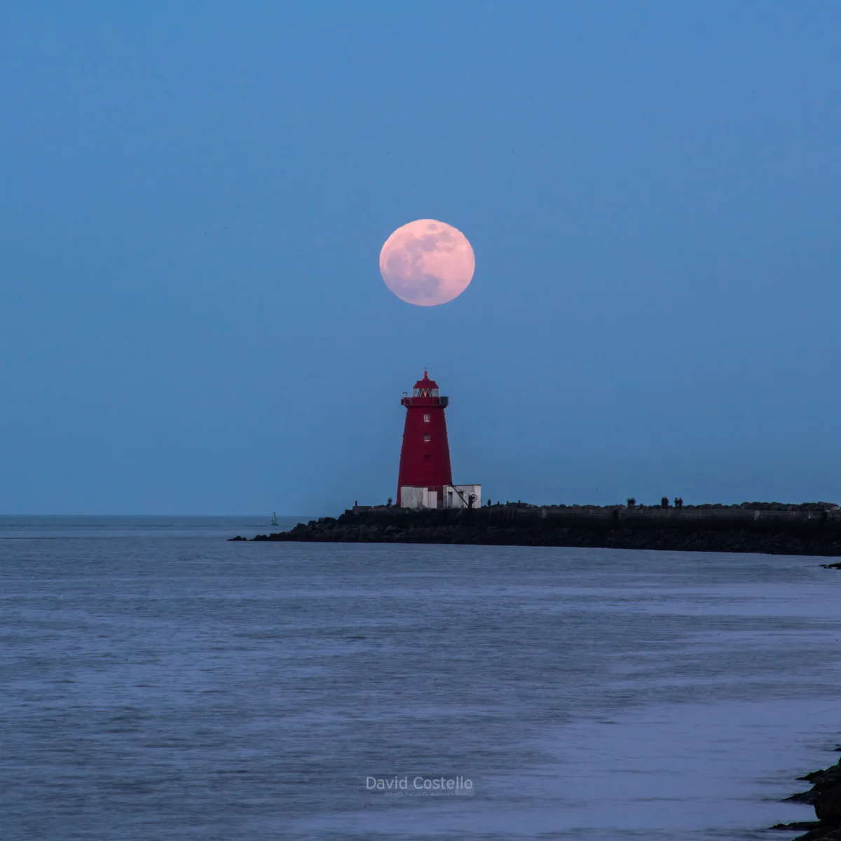 The Full Moon rises above Poolbeg Lighthouse on a beautiful crisp spring evening along the Great South Wall in Dublin.