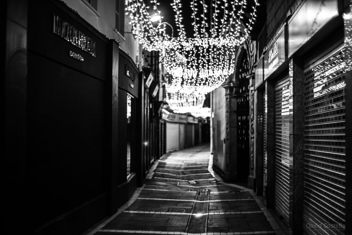 A black and white print of Johnson's Court on Christmas Night with the lights shimmered along the lane.