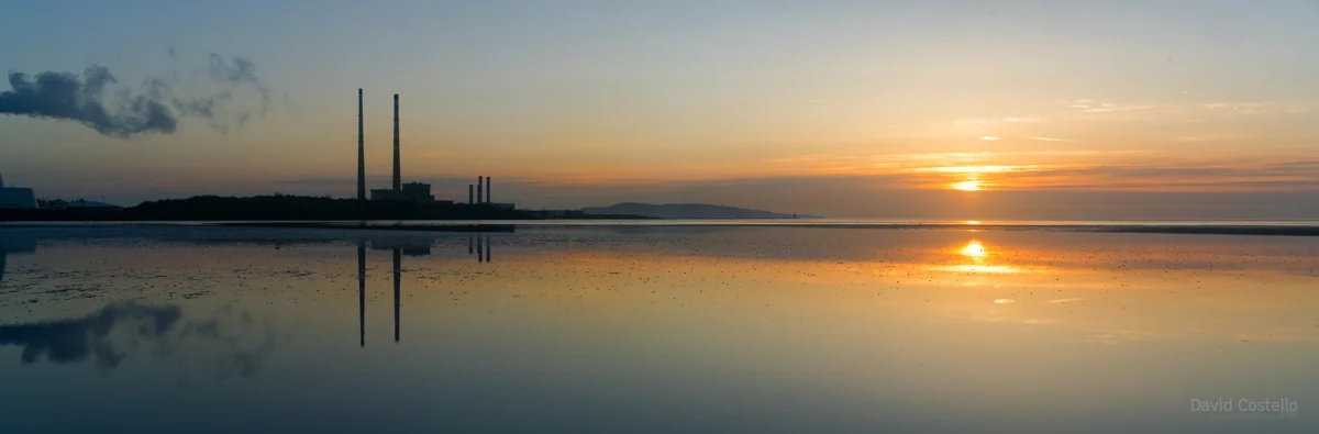 a very wide panoramic view of the sun rising over dublin bay while reflecting in the water