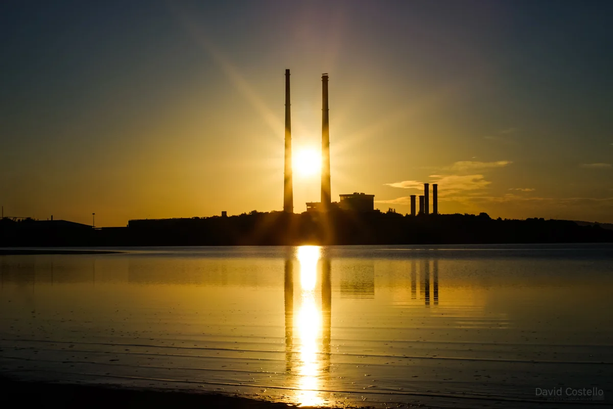 The sunrise between the Pigeon House Chimneys from Sandymount Strand while reflecting in the water.