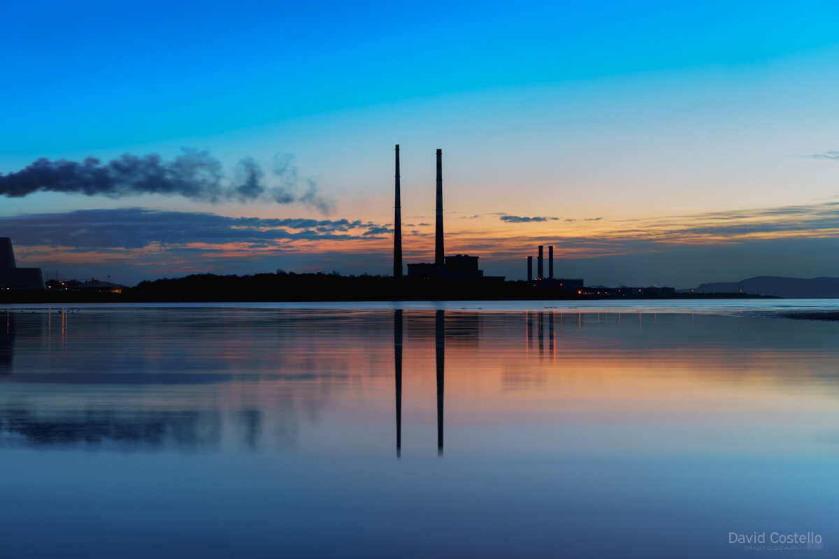 A dawn silhouette of the Dublin Towers reflecting on the peaceful waters of Sandymount Strand in spring.