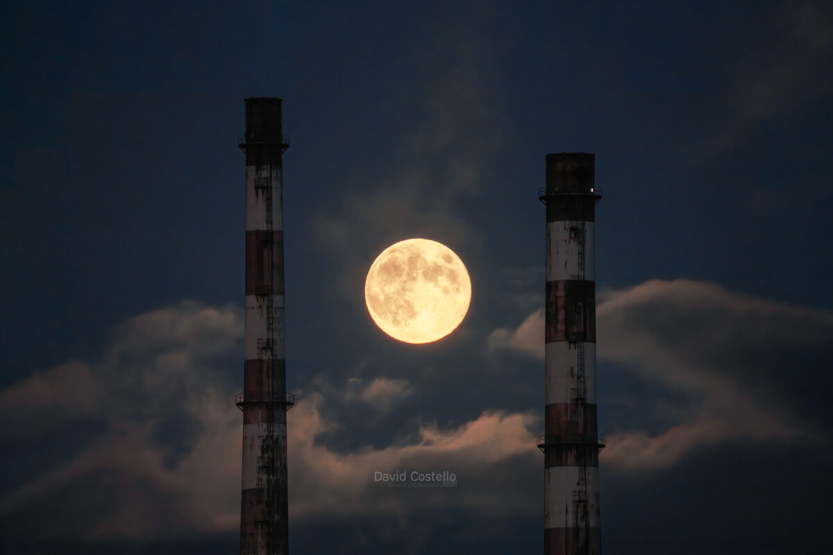 A close up zoom of the Poolbeg Chimneys in the moonlight and the full moon.