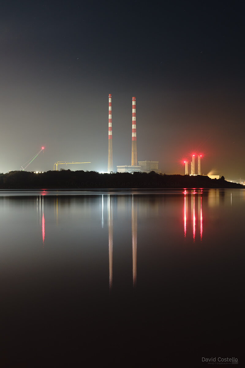 The repainted Poolbeg Chimneys reflect across the smooth waters of Sandymount Strand on a misty November night in Dublin.