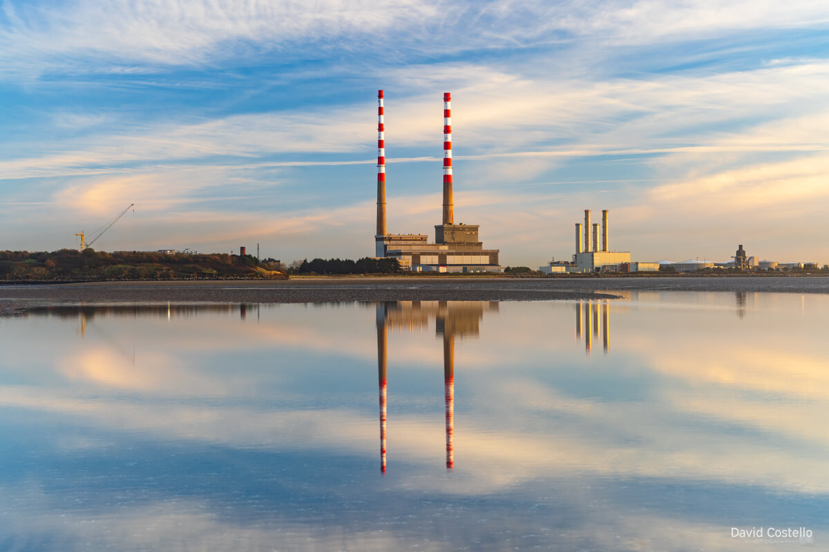 The iconic newly painted Poolbeg Chimneys as they reflect across the incoming tide on Sandymount Strand at sunrise.