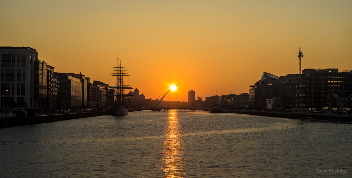 As the sun starts to set down the center of The River Liffey it seems to hang from the Samuel Beckett Bridge...