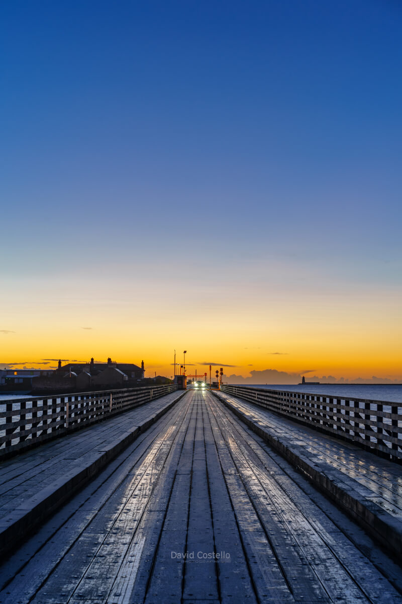 A frozen winter dawn on Clontarf’s Wooden Bridge, the frozen wooden surface glowing beneath a golden-to-blue Dublin sky.