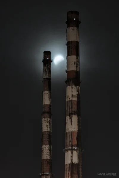 The lunar eclipse dimmed through the mist sits between the Dublin Towers at Poolbeg.