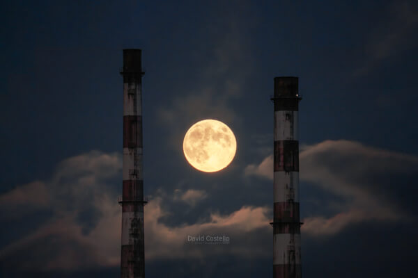 A close up zoom of the Poolbeg Chimneys in the moonlight and the full moon.