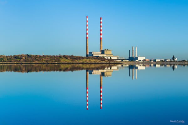 Poolbeg Chimneys reflect in the still water beneath a clear blue sky on a beautiful day in Dublin Bay, Ireland.