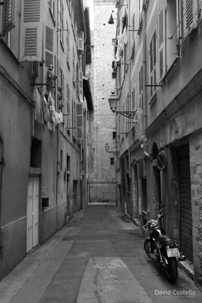 A back street in Nice with a motorbike parked and washing hanging from louvre shutters in black and white.