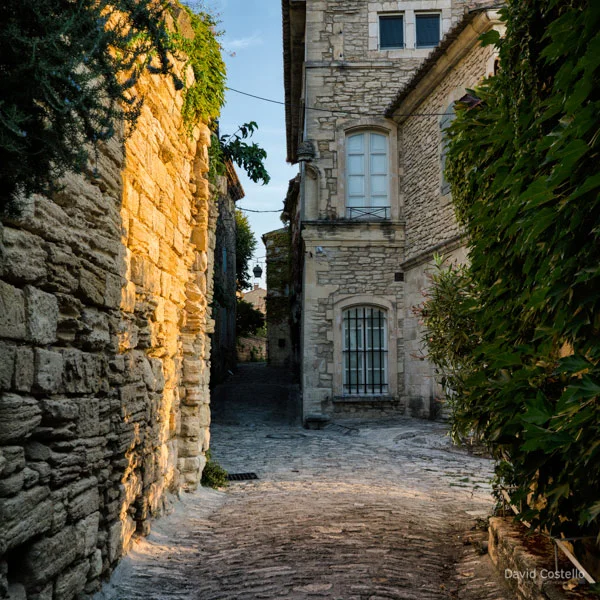 The sunrise against a medieval wall in Gordes and a house in the background with shutters closed.