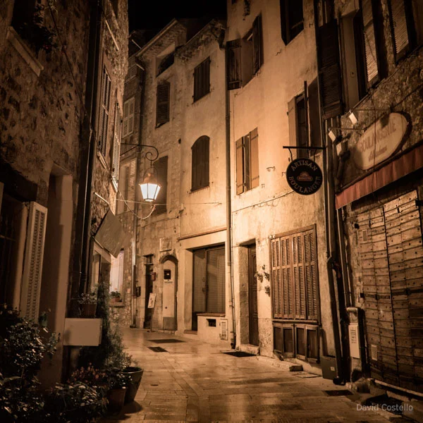 A single lantern lights up the closed boulangerie and the street in Vence at night time.